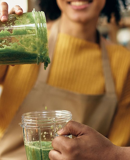 Frau schüttet gesunden Smoothie in ein Glas in der Hand eines Mannes.