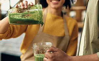 Frau schüttet gesunden Smoothie in ein Glas in der Hand eines Mannes.
