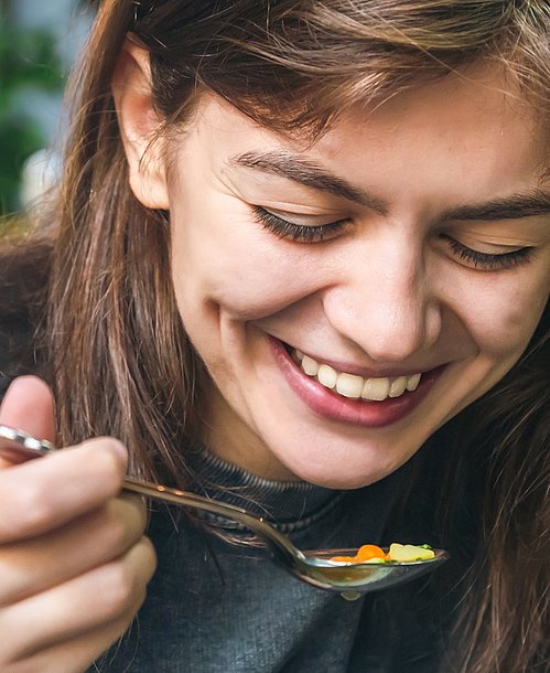 Suppen sind bei Erkältungen eine echte Wohltat. Frau isst Suppe und lacht dabei.