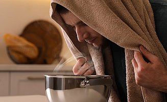 Mann mit Bronchitis inhaliert Kochsalzlösung am Küchentisch. 