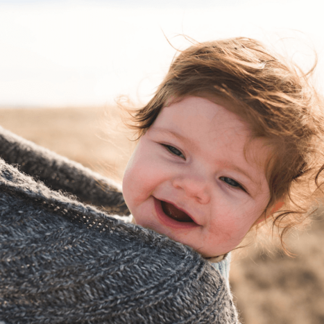 Baby in einem Tragetuch lacht in die Kamera. 