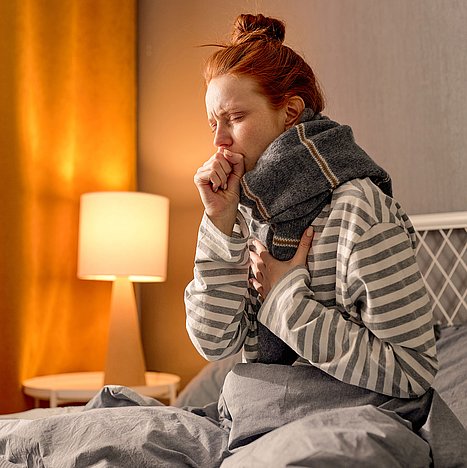 Produktiver Husten ist feucht und mit Schleimauswurf. Frau liegt im Bett und hat Husten mit Schleim.