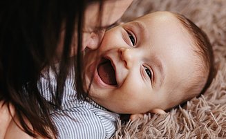Mutter spielt mit lachendem Baby auf einem Teppich.