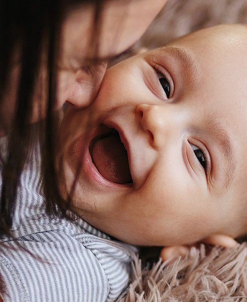Mutter spielt mit lachendem Baby auf einem Teppich.