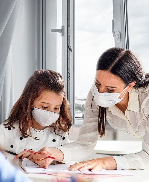 Aufnahme von einem Kind und einer Lehrerin mit Maske